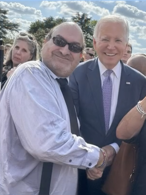 White man with sunglasses shaking hands with President of the United States Joe Biden. 